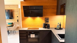 Une cuisine moderne avec un plafond en bois, des appareils électroménagers intégrés et un coin repas visible au fond.