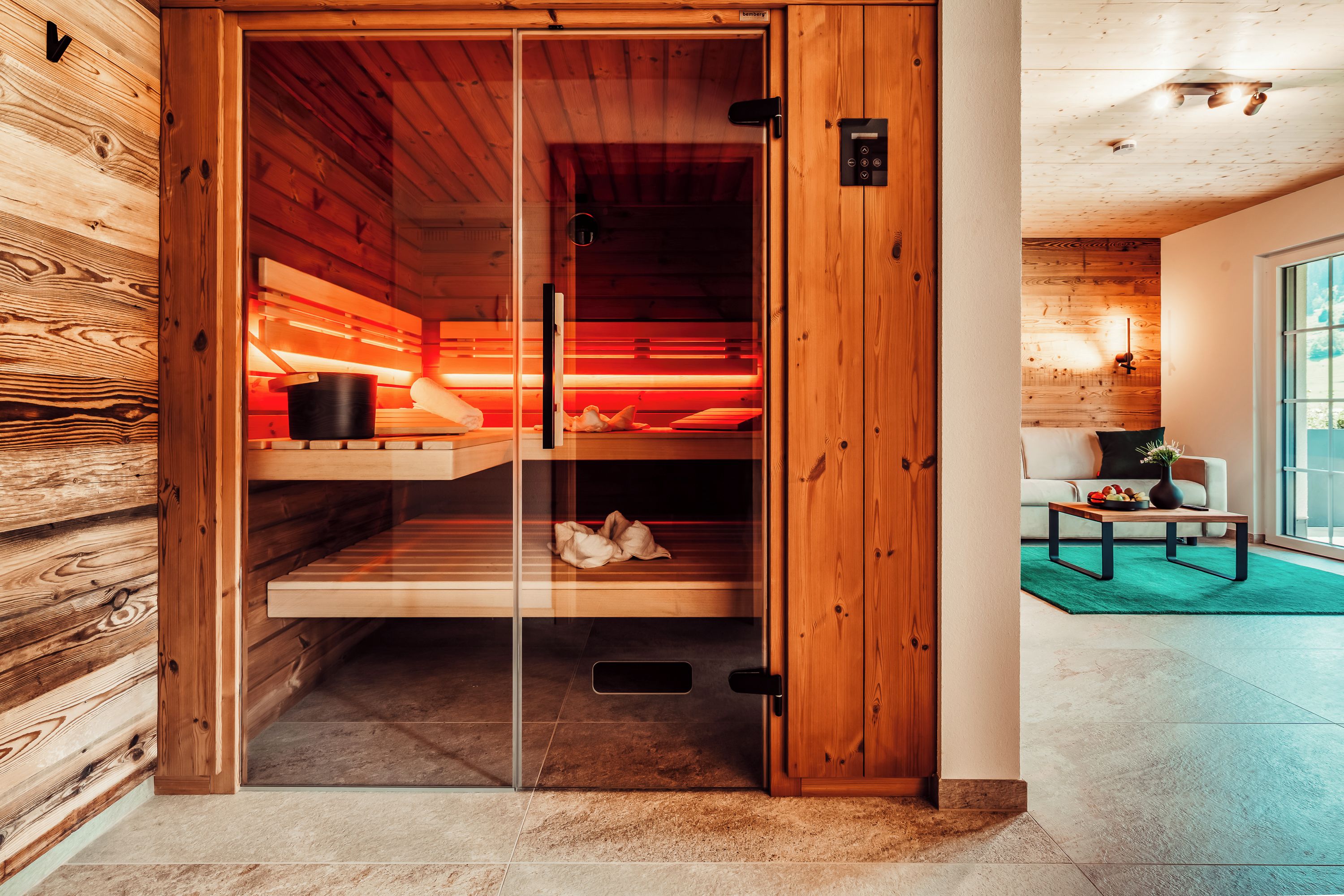 Sala de sauna com paredes de madeira, porta de vidro e painel de controle.