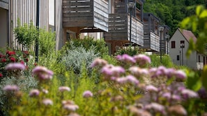 A modern building with wooden balconies, surrounded by lush greenery and flowers. - Stay in Les Eyzies With Pool (Les Eyzies)