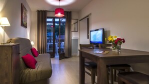 A modern living room with a sofa, a dining table, a TV, and a view through a glass door. - Stay in Les Eyzies With Pool (Les Eyzies)