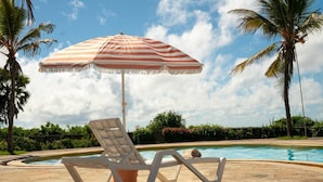 A poolside area with a striped umbrella, lounge chairs, and palm trees. - Creek Side, Ocean View 5-bedroom villa, with a private Coastal feel in Mombasa (Mombasa)