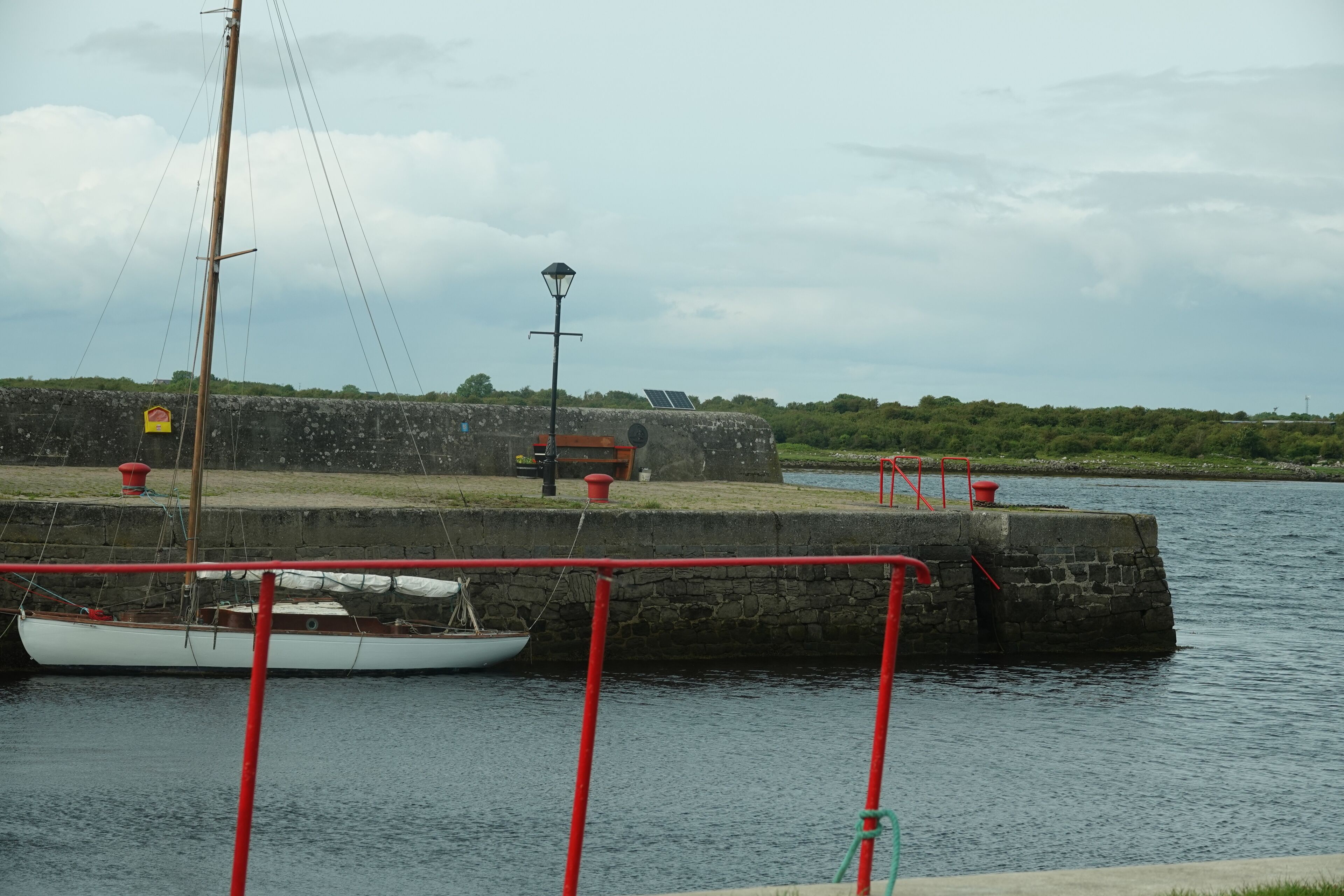 A calm waterfront with a dock, a small boat, and a stone wall.