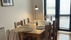 A dining area with a wooden table set for four, a floor lamp, and a framed picture on the wall.