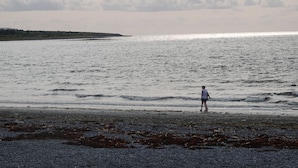 A beach with a person standing on the shore, waves gently lapping at the sand.