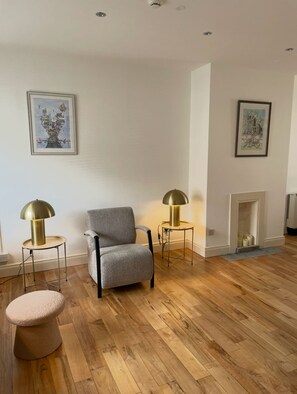 Una sala de estar con un sillón gris, dos lámparas de pie, una chimenea y suelo de madera.