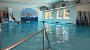 Ein Hallenbad mit einer Bergkuppel-Wandmalerei und durch großen Fenster weiter Blick zum Himmel.