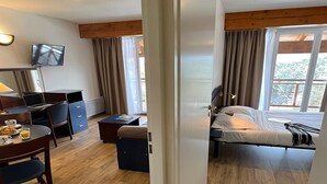 Ein Hotelzimmer mit Bett, Schreibtisch mit Laptop, Stuhl, kleinem Tisch mit Getränk und Wand-Fernseher.