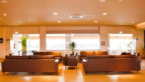Eine geräumige Lobby mit ledernen Sofas, die in einer U-Form angeordnet sind, ein großes Fenster für natürliches Licht und ein sichtbarer Feuerlöscher an der Wand.