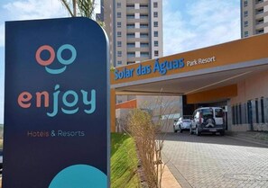 A sign for 'enjoy Hotels & Resorts' and 'Solar das Águas Park Resort' with a parking area and buildings in the background. - SOLAR DAS AGUAS PARK RESORT - OLIMPIA SP (Olímpia)