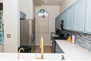 Eine Küche mit Kühlschrank, Herd und Mikrowelle. Es gibt ein Fenster mit Jalousien, ein Waschbecken mit goldenem Wasserhahn und Schränke mit goldenen Griffen.