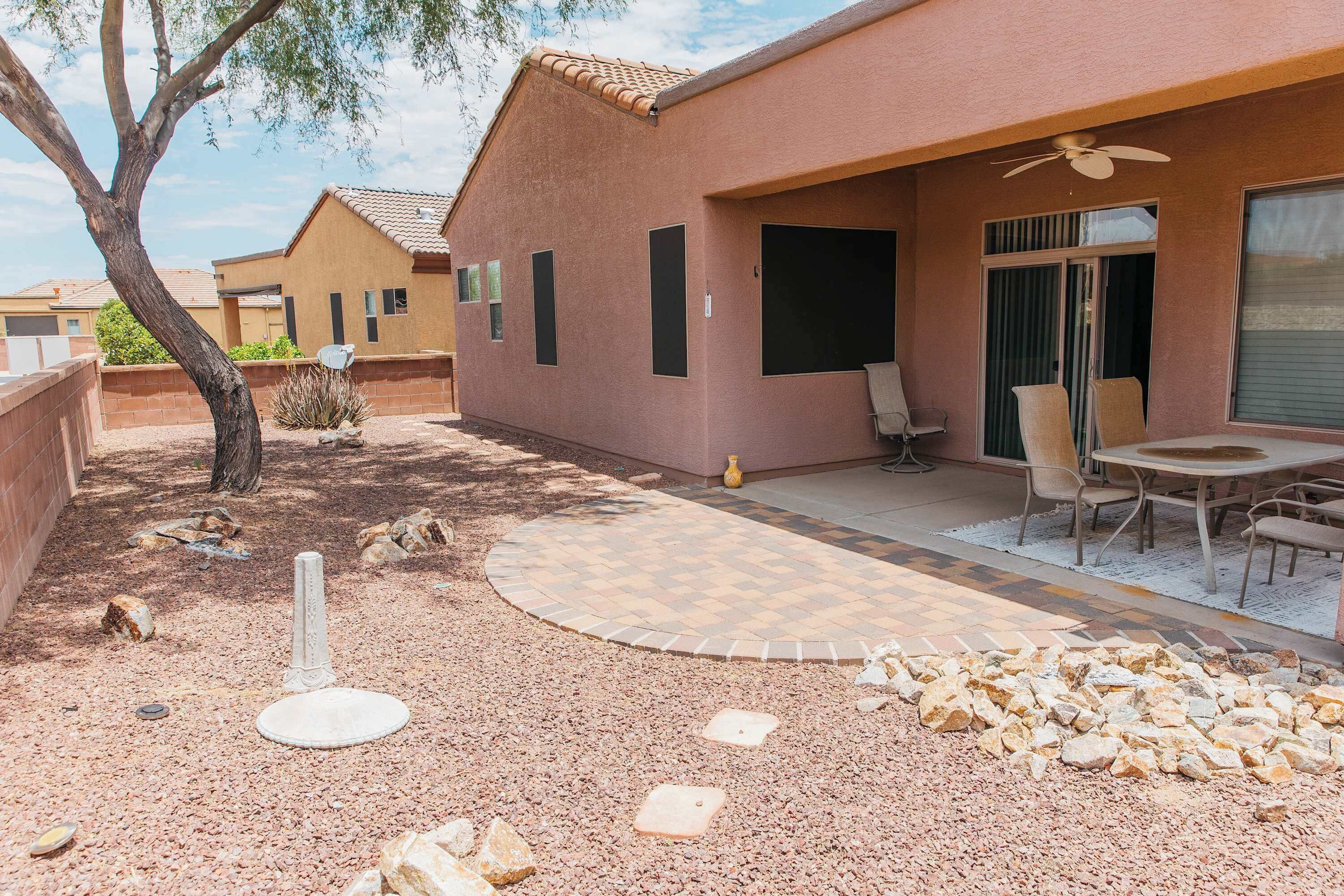 A residential outdoor area with a patio, seating, and a tree.