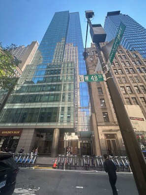 Ein Hochhaus mit Glasfassade, ein Straßenschild für W 48 St und eine Fahrradverleihstation.