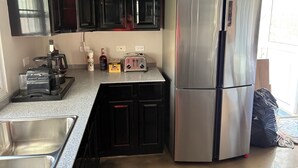 Eine Küche mit dunklen Schränken, einem Edelstahl-Kühlschrank, einem Toaster, einer Kaffeemaschine und einem Spülbecken.