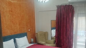 Quarto de hotel com uma cama grande, uma cadeira, um candelabro e uma janela com cortinas.