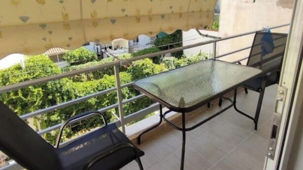 Uma varanda com mesa e cadeiras de vidro, teto trabalhado e vista para o verde.