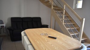 A room with a wooden table, two white chairs, a black sofa, and a wooden staircase. - Gîte Terre d'Ardenne (Le Thour)