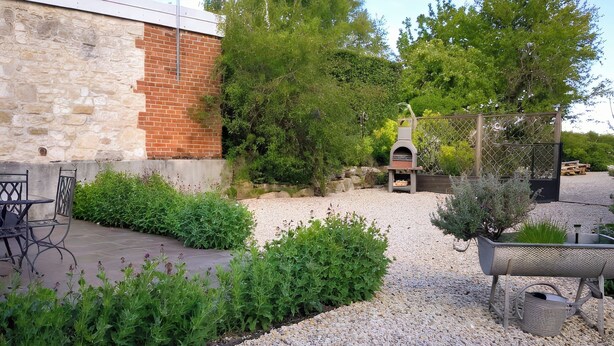 A patio area with a stone wall, a brick wall, a grill, and a seating area with chairs and a table. - Gîte Terre d'Ardenne (Le Thour)