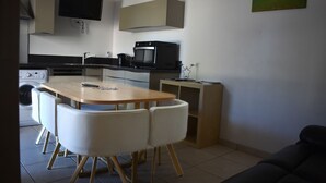 A compact kitchen with a dining table, chairs, a washing machine, and a microwave. - Gîte Terre d'Ardenne (Le Thour)