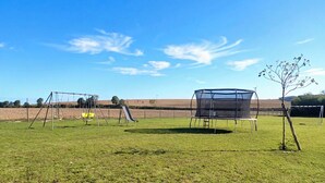 A grassy field with swings, a trampoline, and a tree. - Gîte Terre d'Ardenne (Le Thour)