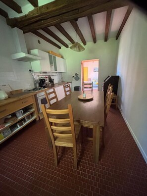 A kitchen with a dining table, chairs, and a brick floor. - Gîte de l'Étang Neuf (Paulnay)
