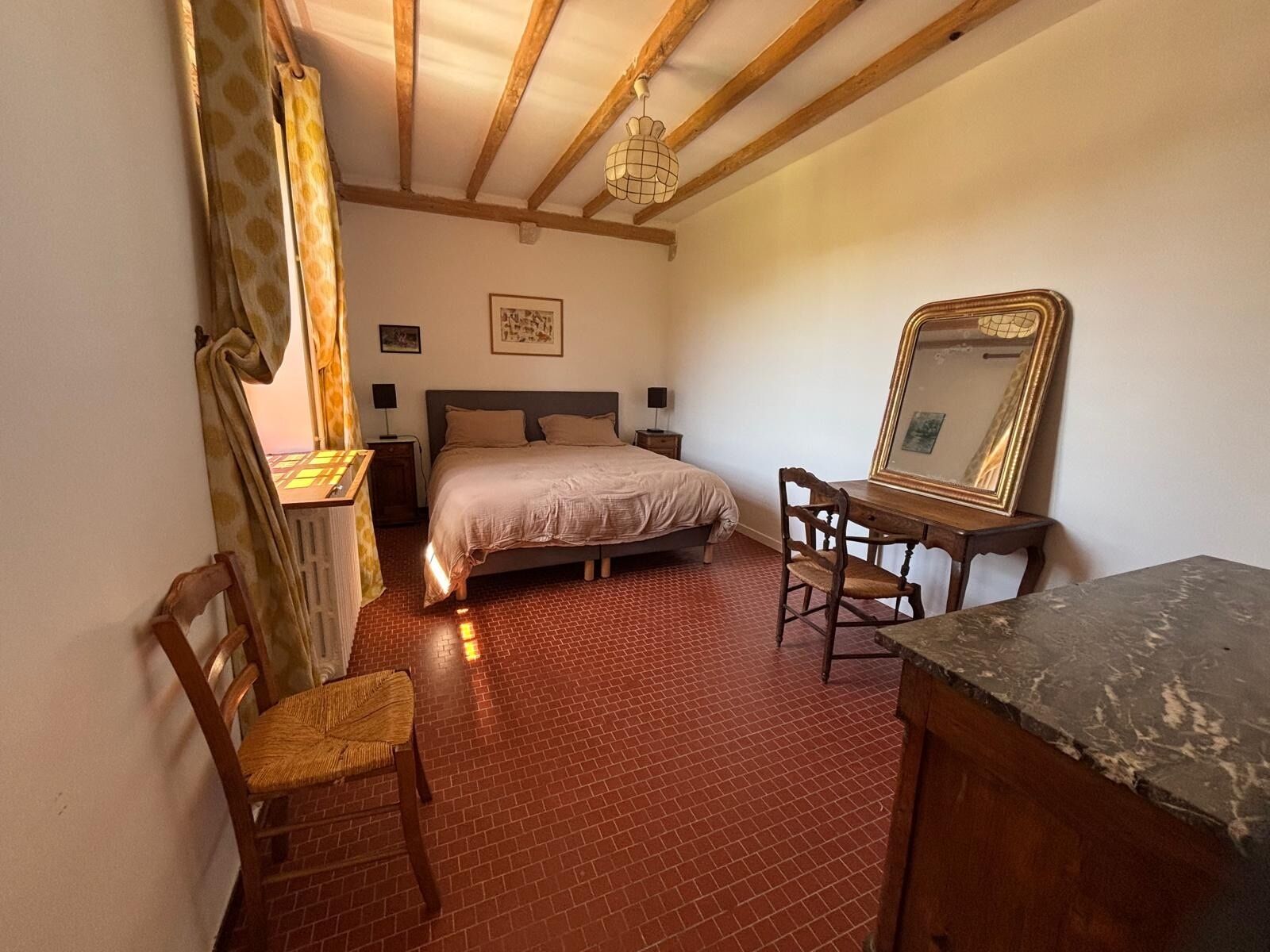 A bedroom with a bed, a desk, a chair, a mirror, and a lamp.