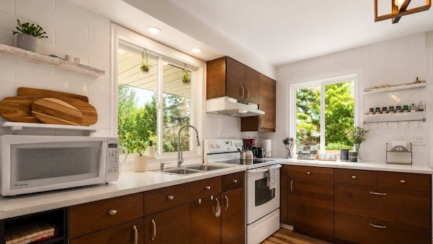 A modern kitchen with wooden cabinets, white countertops, a built-in microwave, and a window providing a view of greenery.