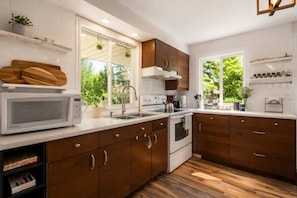A modern kitchen with wooden cabinets, white countertops, a built-in microwave, and a window providing a view of greenery.