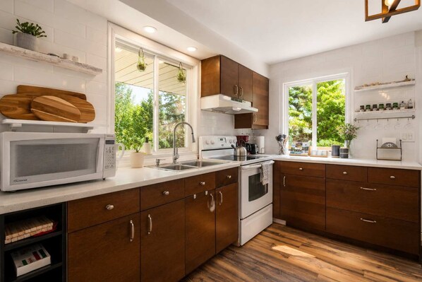 Una cocina moderna con armarios de madera, encimeras blancas, microondas integrado y ventana con vista a la vegetación.