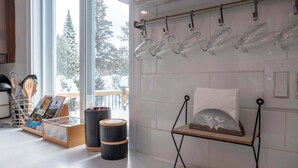 A kitchen with a window view, a hanging glass rack, a wooden shelf with a cushion, and a spice rack.