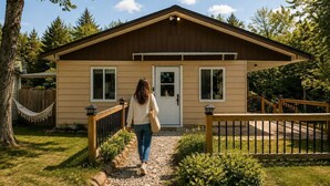 A single-story building with a front door, two windows, a wooden deck, and a hammock.