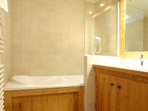 A bathroom with a wooden vanity, a white bathtub, and a large mirror. - Appartment in Vaujany (Les Deux Alpes)