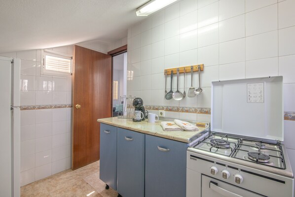 Una cocina con estufa, armarios, cafetera y una ventana con persianas.