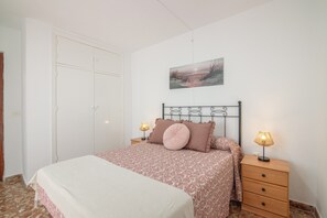Un dormitorio con cama, dos mesitas de noche con lámparas, un armario y un cuadro en la pared.