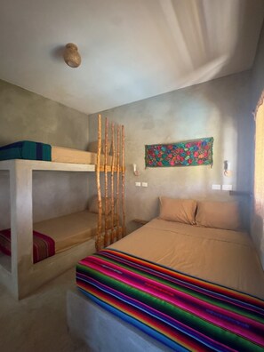 A room with bunk beds, a colorful blanket, a wall hanging, and a ceiling light fixture.