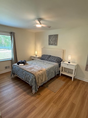 Ein Schlafzimmer mit Bett, Nachttischen, Deckenventilator und einem Fenster mit Vorhängen.