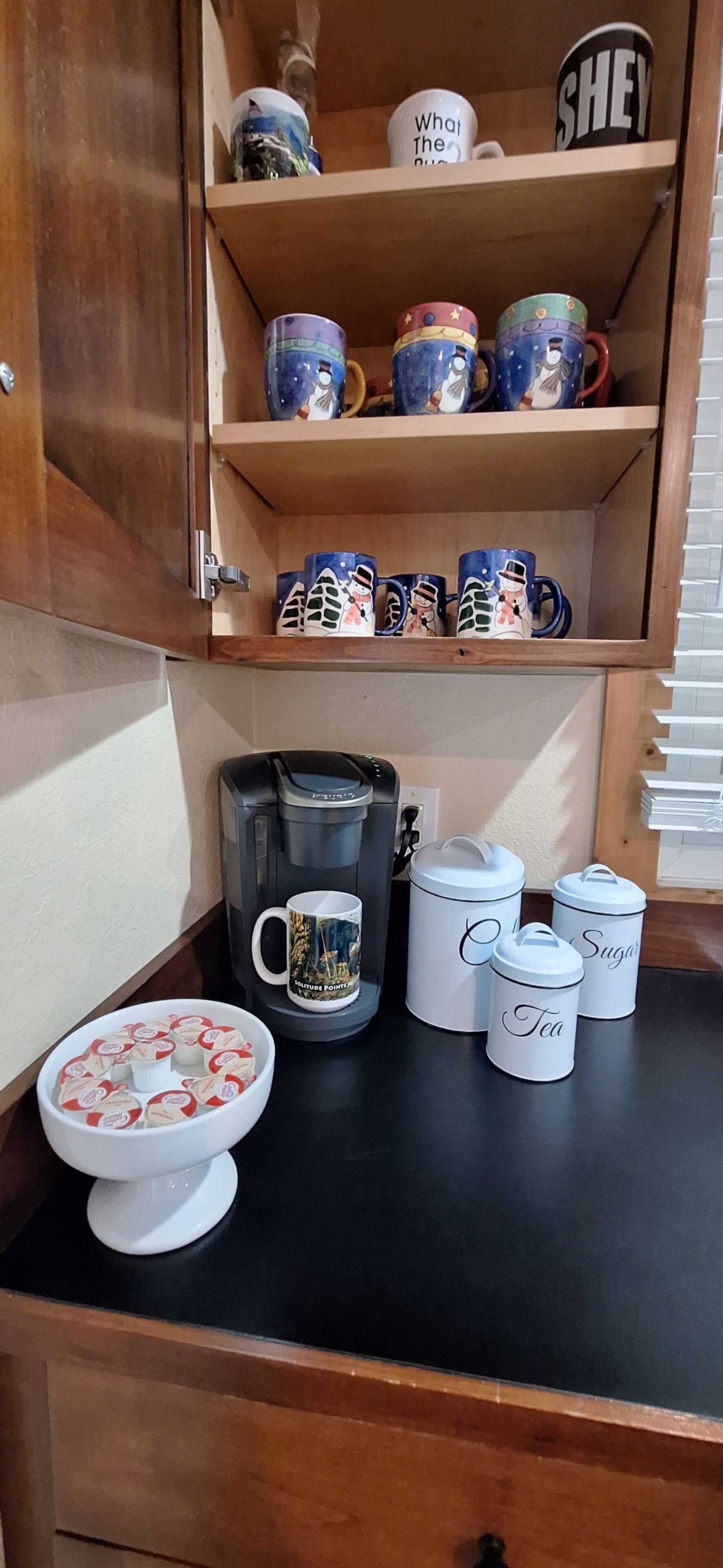 Uma cozinha com cafeteira, recipientes de chá e açúcar, e uma tigela com saquinhos de chá no balcão.