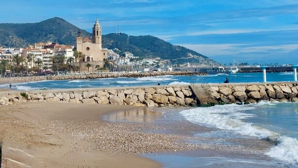 Uma vila costeira com uma igreja imponente, praia de pedras e um muro de pedra que separa a praia do mar.