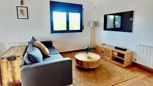 Uma sala de estar com sofá, televisão, janela e teto de madeira.