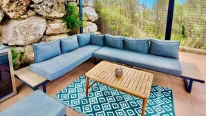 Uma área de estar ao ar livre coberta com parede de pedra, um sofá azul, uma mesa de madeira e um tapete estampado.