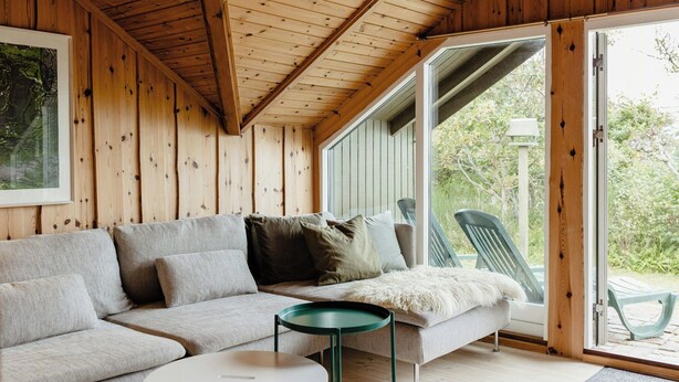 A wooden interior with a sofa, a round table, and a sliding glass door leading outside. - Simple living right next to the sea (Græsted)