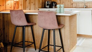 A wooden interior with a kitchen area, two bar stools, a hanging light fixture, and a window. - Simple living right next to the sea (Græsted)