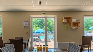 A dining area with wicker chairs, a glass table, breakfast items, and a view of an outdoor pool area. - Spacious Stay for Two Near Vannes (Plescop)