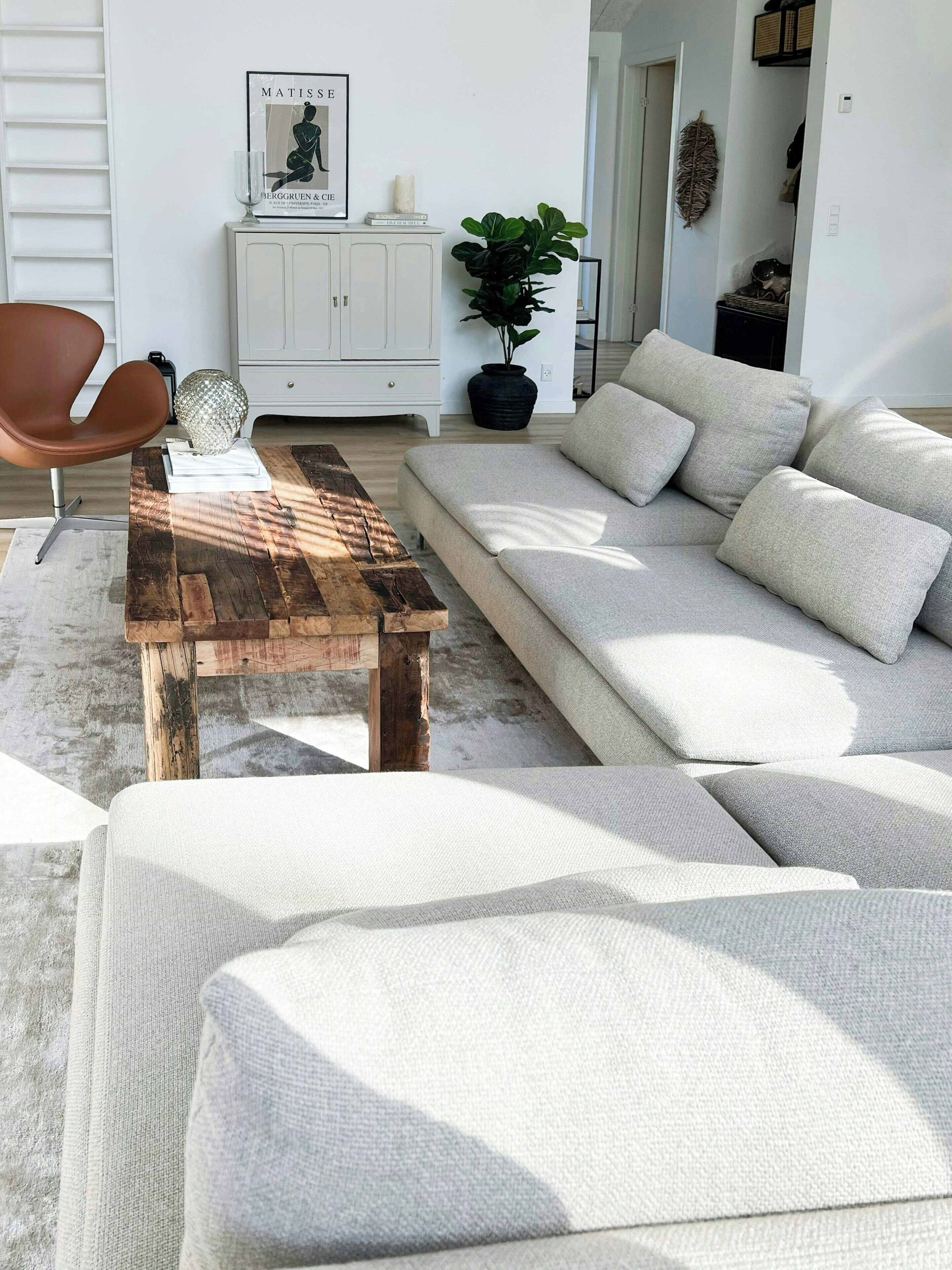 Een moderne woonkamer met een houten salontafel, een beige bank, een witte kast en een kunstwerk in een lijst aan de muur.