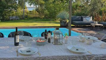 An outdoor dining area with a pool view, a table set with plates, glasses, and a bottle, surrounded by chairs.