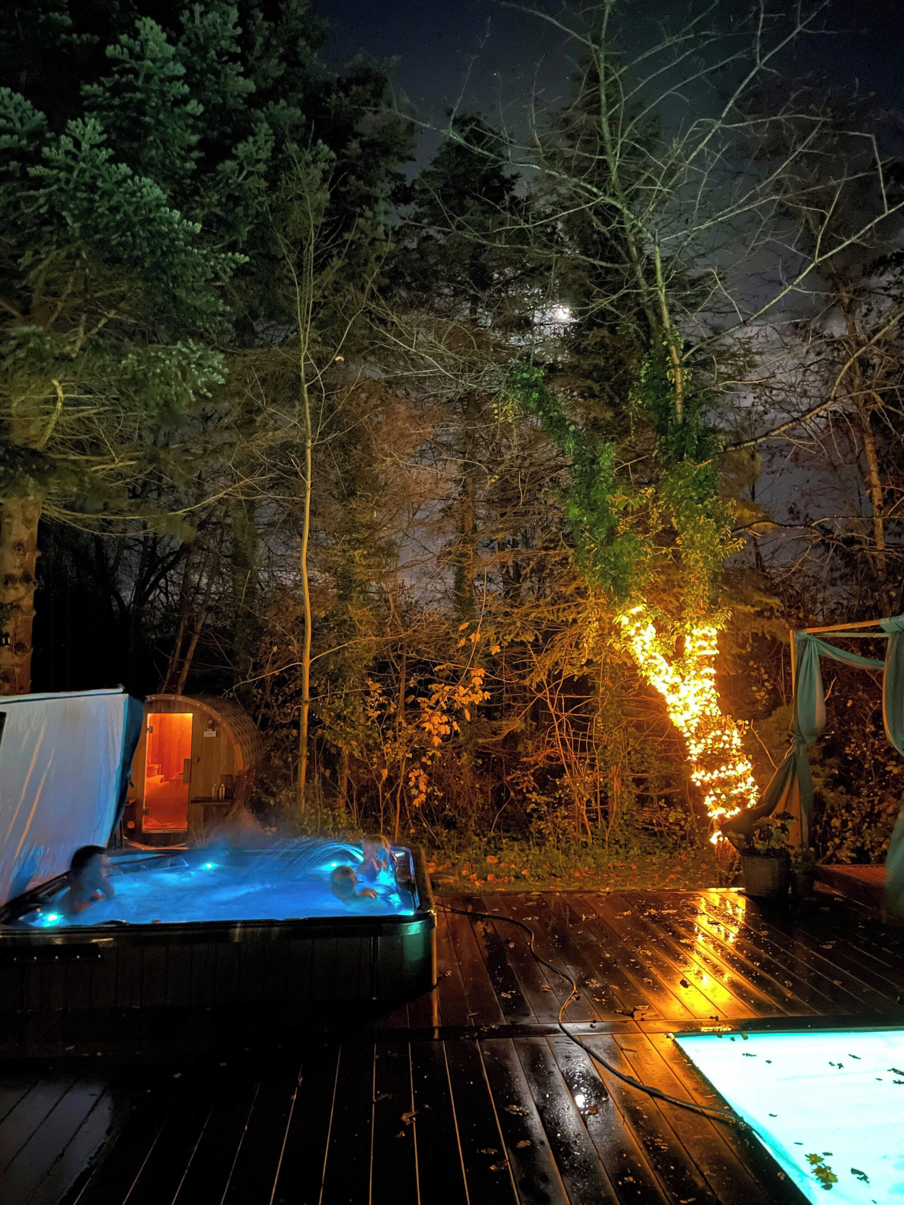 A hot tub on a wooden deck with a tent and a small building in the background.