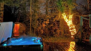 A hot tub on a wooden deck with a tent and a small building in the background.