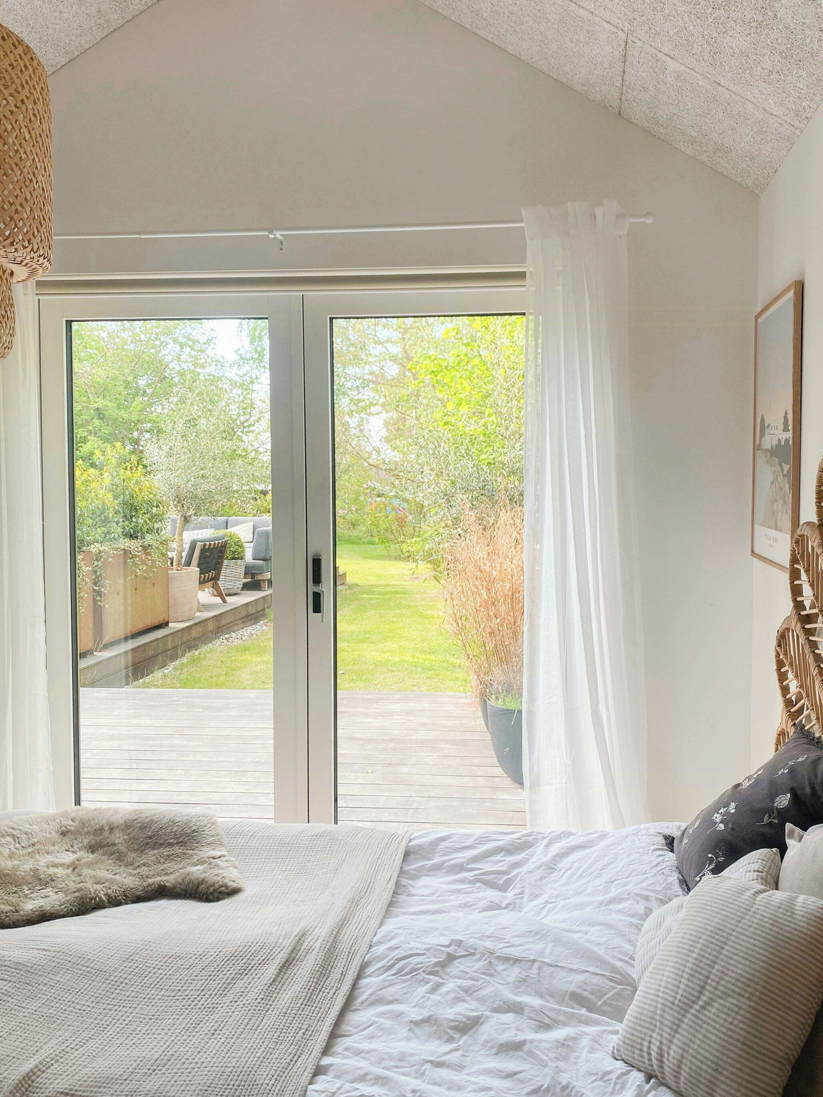 Une chambre à coucher avec un lit, une grande fenêtre donnant sur un jardin et une porte menant à l’extérieur.