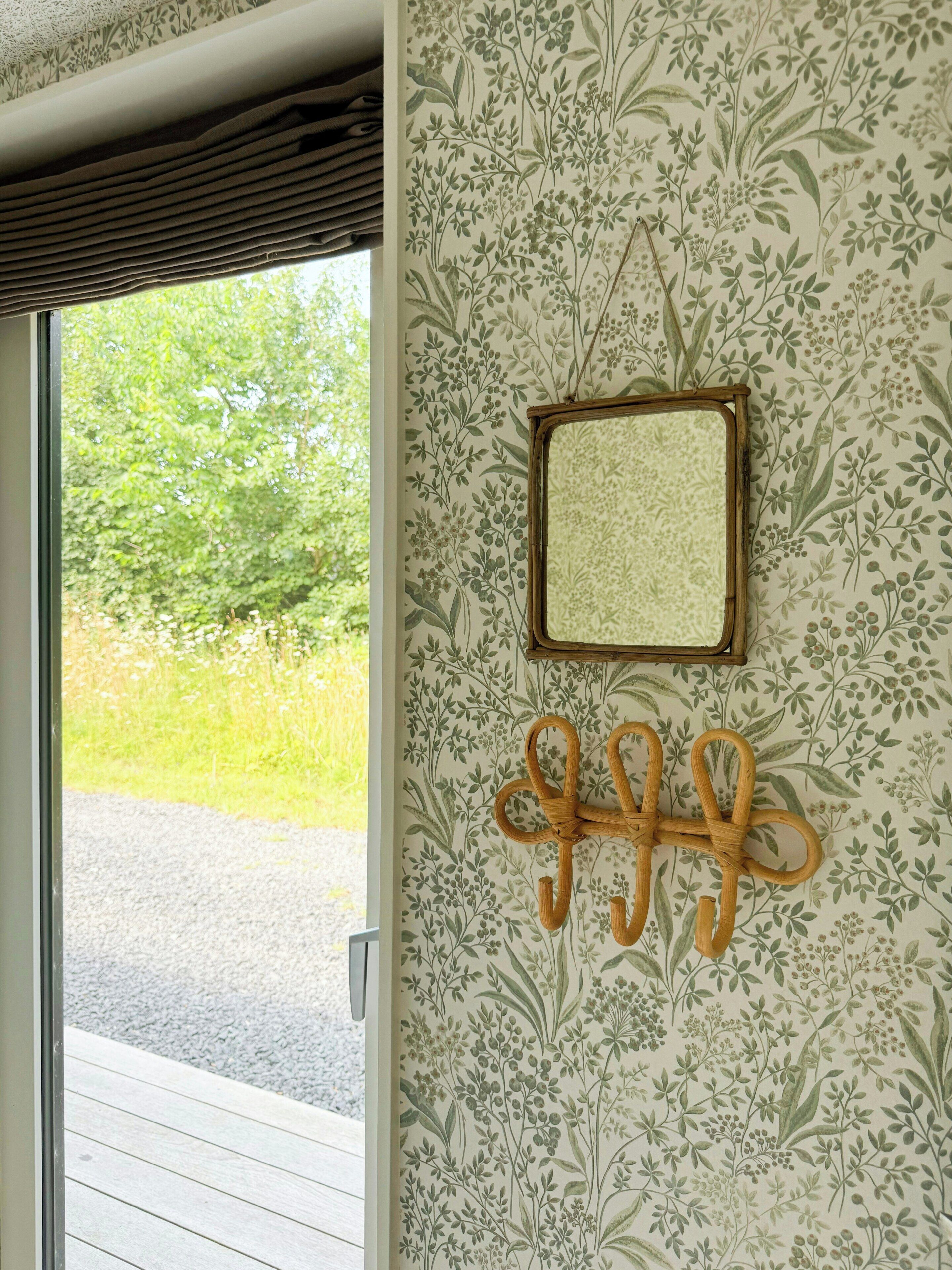 A room with a patterned wallpaper, a framed mirror, and a wooden wall decoration.