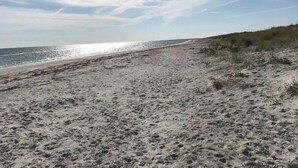 En sandstrand med fodspor, klar himmel og fjerntliggende vand.