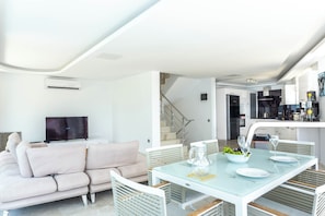 A modern living room with a sofa, a dining table set for two, and a kitchen area visible through an open doorway.